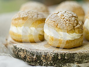 Gourmet French Shu cake. Gourmet custard dessert with creamy white cream on a wooden saw. Rustic style. Closeup