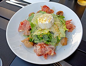 A gourmet green salad plate served with prosciutto and ricotta white cheese