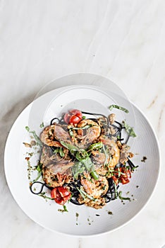 Gourmet grilled prawn and vegetables on black squid ink pasta