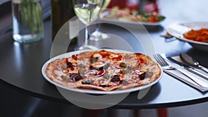 Gourmet pizza alongside two wine glasses and a bottle of wine on a black table