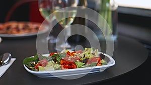 Gourmet salad alongside two wine glasses and a bottle of wine on a black table