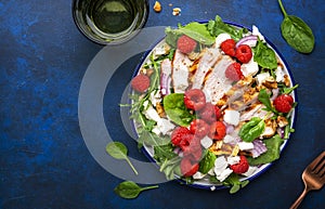 Gourmet salad with raspberries, grilled chicken, feta cheese, red onion, walnuts, spinach and mixed herbs, blue table background,