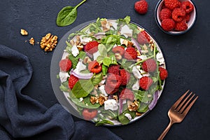 Gourmet salad with raspberries, white cheese, red onion, walnuts and mixed herbs, black table background, top view