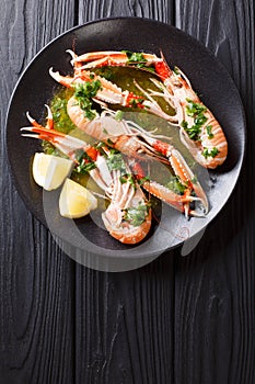 Gourmet seafood scampi or langoustine or Norway lobster are served on a black plate with sauce and lemon. Vertical top view