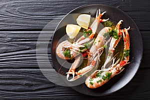 Gourmet seafood scampi or langoustine or Norway lobster are served on a black plate with sauce and lemon. horizontal top view