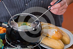 Gourmet Swiss fondue dinner with assorted cheeses and a heated pot of cheese fondue, man holding with a fork dipping a