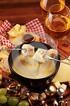 Gourmet Swiss fondue dinner on a winter evening with assorted cheeses on a board alongside a heated pot of cheese fondue with two