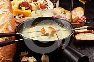 Gourmet Swiss fondue dinner on a winter evening with assorted cheeses on a board alongside a heated pot of cheese fondue with two