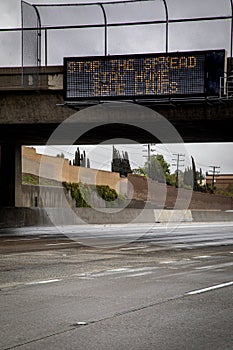 Government digital freeway sign at overpass with message stating â€œStop The Spread ,Stay Home, Save Livesâ€ with no cars