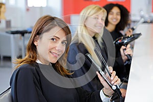 gowned women in hairdresser chairs holding different electrical haidressing appliances