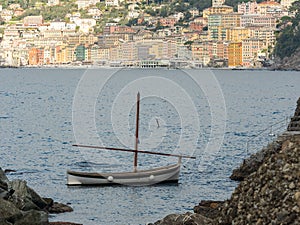 Gozzo armed with lateen sail anchored in a tranquil bay next to the coast. the famous city of