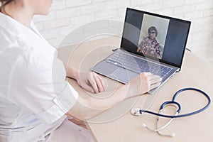 Gp hosts an online appointment with an elderly quarantined patient at home. Female doctor at the desk talking to an photo