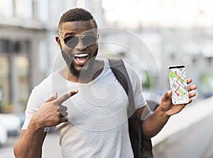 Gps App. Cheerful Black Man Pointing At Smartphone With Opened Navigation Maps