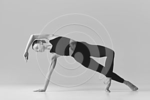 Grace. Black and white photography. Young slim, fit girl training, doing stretching exercises over studio background