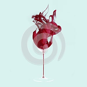 Grace. Creative artwork. Red wine texture made of red dye, liquid with drops and splashes. One wine glass isolated on