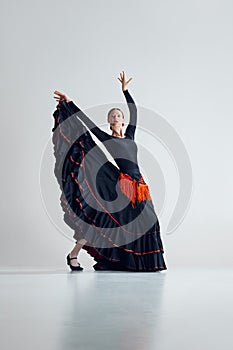Grace of flamenco dance. Artistic talented woman in stylish dress performing flamenco against grey studio background