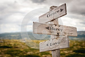 grace mercy love text engraved on old wooden signpost outdoors in nature