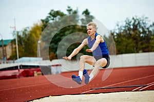 Graceful arch as a runner jumps into sand. Dynamic portrait of athletic man, professional sportsman doing perfect long