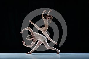 Graceful, artistic couple, man and woman, professional ballet dancers performing against black studio background