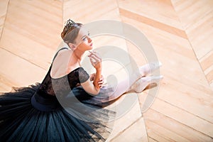 Graceful ballerina in black tutu rests sitting on floor with her back to the camera