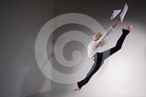 A graceful ballerina in a business suit throws documents in the studio. Business woman dance barefoot on a white