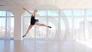 Graceful ballerina dancer performing a jump in white studio