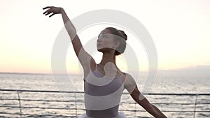 A graceful ballerina dancing ballet elements outside with sea on the background. Caucasian ballet dancer in white tutu