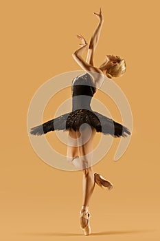 Ballerina Dancing in Classic Tutu Skirt. Ballet Dancer in Black Dress Balance at One Leg over Beige Studio Background