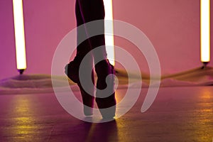 Graceful ballerina is dancing a classical ballet in white pointe shoes against a background of bright neon lights