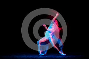 Graceful ballerina dancing on dark background in mixed neon light. Grace, movement, action and motion concept. Looks