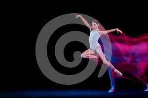 Graceful ballerina dancing on dark background in mixed neon light. Grace, movement, action and motion concept. Looks