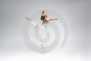 Graceful ballerina dancing in white dress on grey background