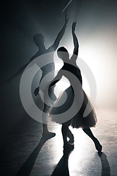 Graceful ballerina and her male partner dancing elements of classical or modern ballet in dark with floodlight backlight