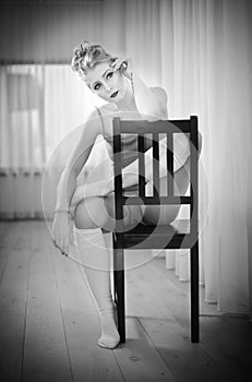 Graceful ballerina resting on chair. Black and white portrait of gorgeous ballet dancer sitting. Blonde ballerina relaxing