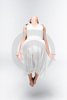 Graceful ballerina in white dress dancing on grey background