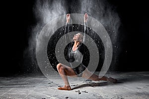 Graceful ballet dancer woman dancing and sprinkle flour on black background