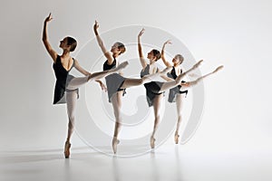 Four graceful ballet dancers, teens in black leotards and pointe standing in md-pose, practicing against grey studio photo