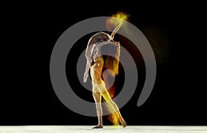 Graceful, beautiful couple, man and woman, ballet dancers performing against black studio background with colorful power