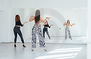 Graceful dancing women doing elegant dance movements in white color spacious hall with big mirror wall.People's expressions