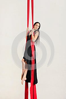 Graceful female aerialist performing dance on red hanging silks