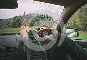 Graceful female palms holding the hot tea thermos mug. She sitting on co-driver seat inside modern car,putting legs on dashboard photo