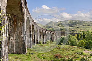 Graceful Glenfinnan Viaduct spans lush Scottish Highlands, rolling hills and greenery under a dynamic sky