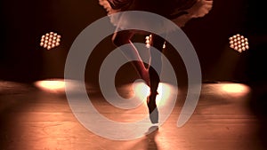 Graceful legs of a ballerina in white pointe shoes. Ballerina shows classic ballet pas. Shot in a darkness on spotlights