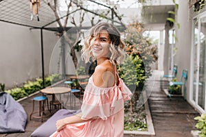 Graceful short-haired girl looking over shoulder in cozy street restaurant. Outdoor shot of pleasan