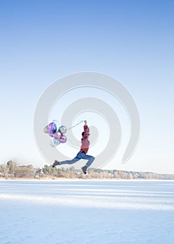 graceful slender pretty teenage girl  holding many colorful balloons in her hands  jumping over the snowy ground