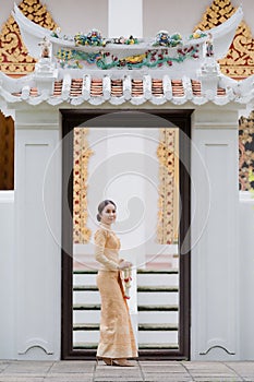 A graceful Thai woman in Thai dress adorned with precious jewelry holds a flower garland through the beautiful ancient Thai temple