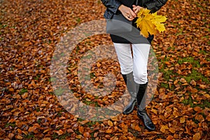 Graceful woman feet in elegant boots walking on fall leaves in an autumn forest