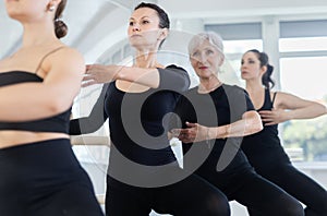 Graceful woman mastering passe ballet move at barre with group photo