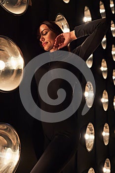 Graceful woman touching neck, while posing in bulbs lights.