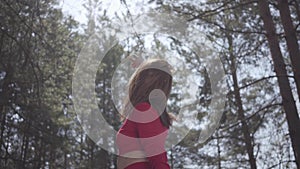 Graceful womans body in red dress in the forest. Lady raises hand in the sky